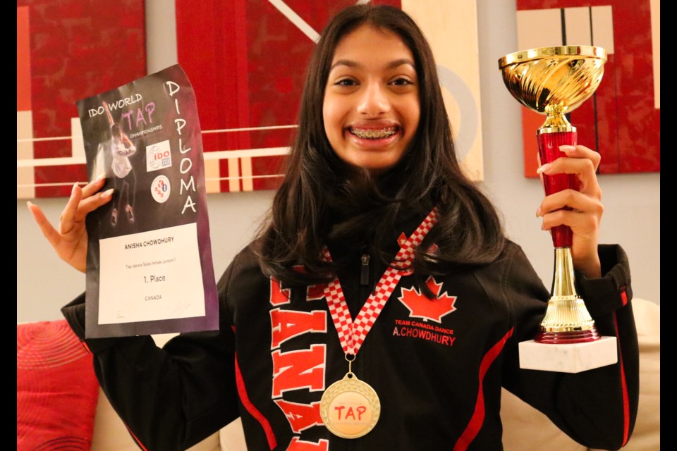 Photo of Anisha Chowdhury smiling, holding gold trophy and a certificate with a gold medallion around her neck.