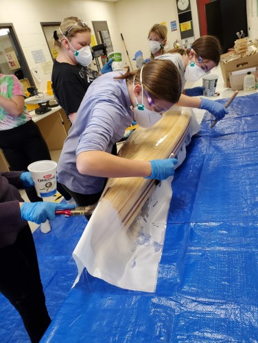 This photo features a group of students applying epoxy to the model canoe.