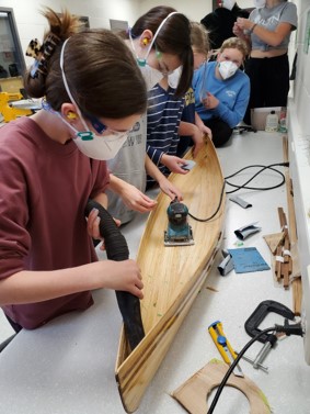 This phot features a group of students sanding down the model canoe.