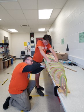 This photo features teacher and young male studentd building the frame of the canoe.