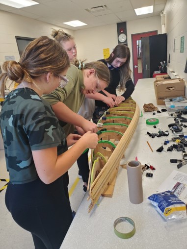 This photo features a group of female students laying the wooden strips of the canoe.