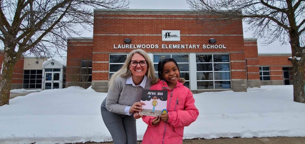 This photo features Laurelwoods principal, Lori Shilvock and Amaya James holding Amaya's book 'Afro, No!' while standing outside Laurelwoods Elementary School.