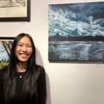 This photo shows Annie Y standing in front of their artwork smiling.