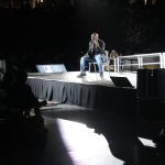 This photo features a man on stage sitting down.