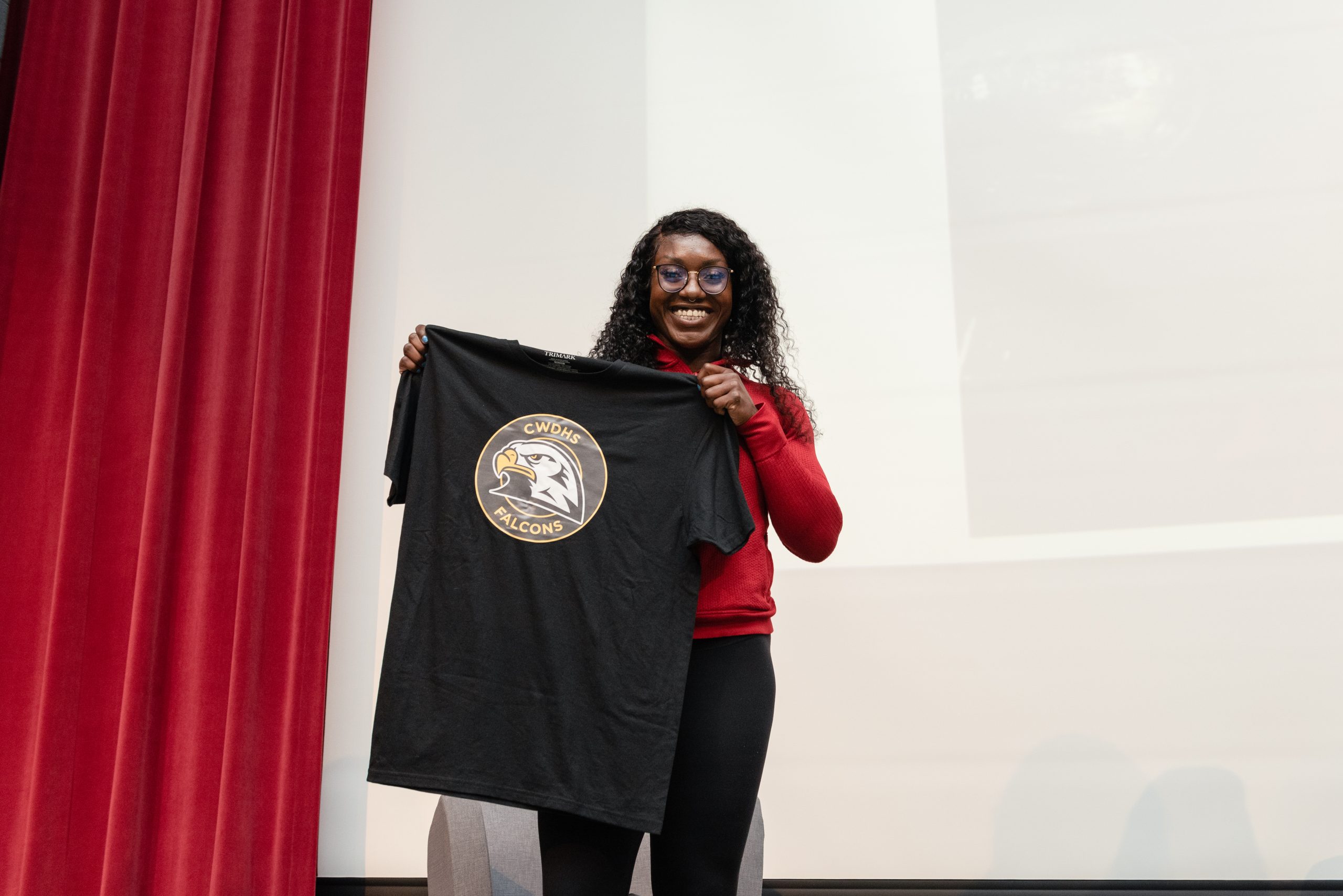This photo features Olympian, Cynthia Appiah holding up a Centre Wellington District High  School t-shirt to her body.