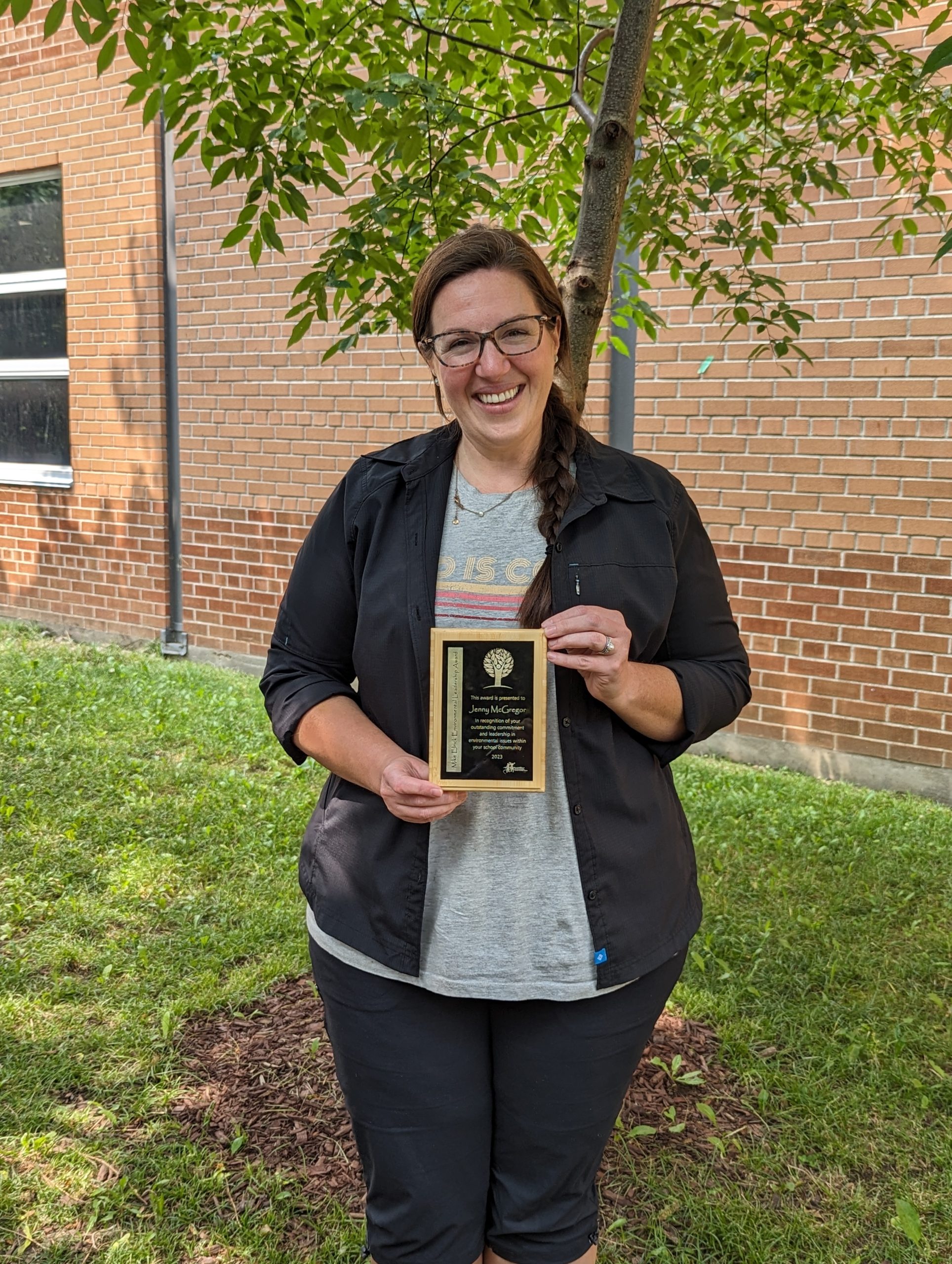 This photo features Jenny McGregor posing outside, holding the Mike Elrick Environmental Leadership award.
