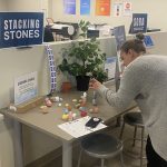 This photo features a woman stacking stones on top of one another on a table.