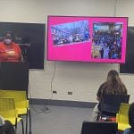 This photo features a femme individual giving a presentation to a group of students.